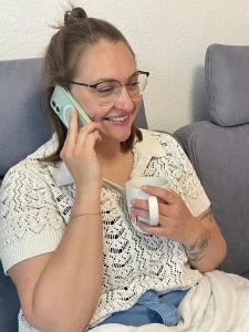 Frau sitzt entspannt mit einer Tasse Tee auf dem Sofa und führt ein telefonisches Gespräch während einer medialen Beratung.