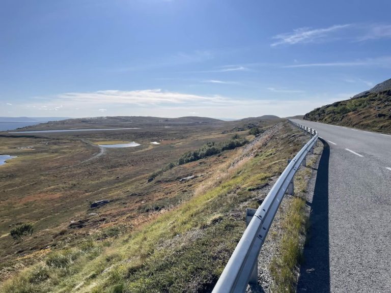 Straße durch die weite, karge Landschaft Nordnorwegens unter blauem Himmel.